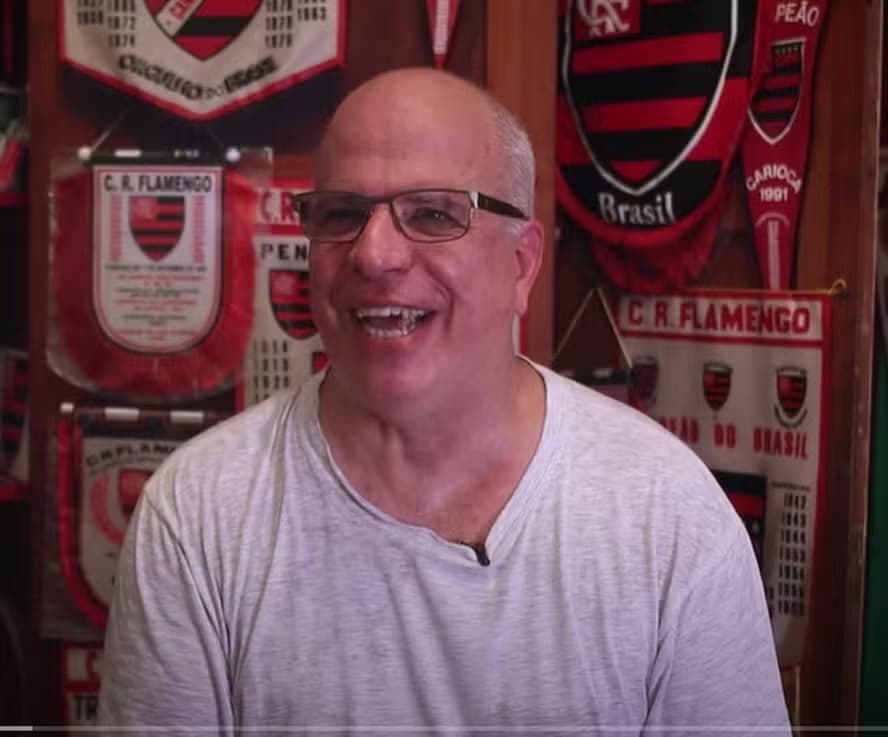 Eduardo Vinicius sorri, atrás, diversas flâmulas do Flamengo que fazem parte do acervo