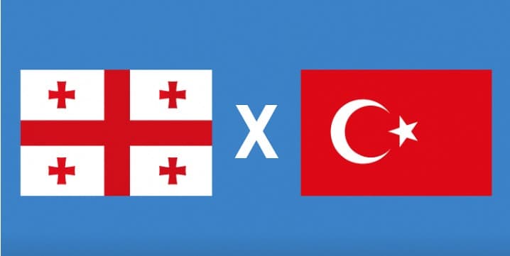 Bandeiras da Geórgia e da Turquia lado a lado com um "X" no centro sobre fundo azul, simbolizando o confronto nas Eliminatórias da Copa do Mundo 2026.