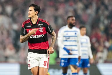 Pedro aponta para o escudo do Flamengo ao comemorar gol sobre o Cruzeiro; ao fundo, Gerson lamenta