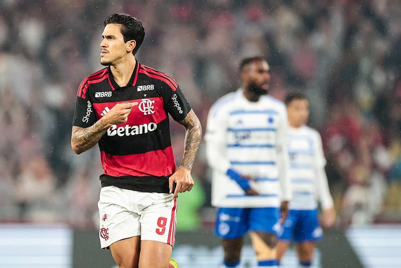 Pedro aponta para o escudo do Flamengo ao comemorar gol sobre o Cruzeiro; ao fundo, Gerson lamenta