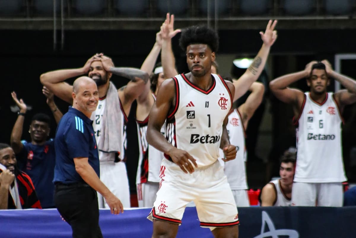 Gui Deodato sério após ponto contra Paulistano; ao fundo Oveja e companheiros celebram cesta do FlaBasquete