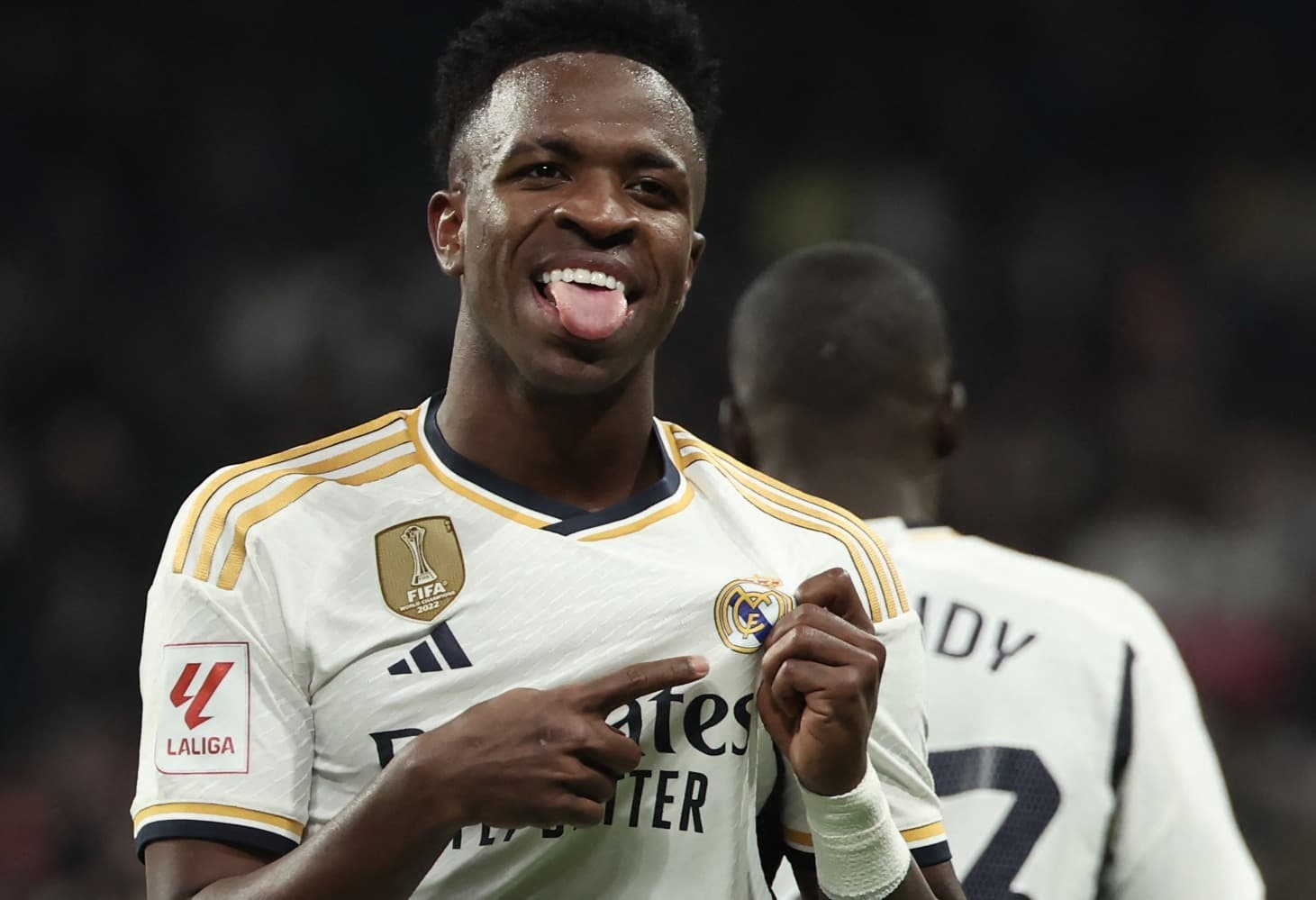 Vinícius Júnior sorri e aponta para o escudo do Real Madrid ao comemorar gol