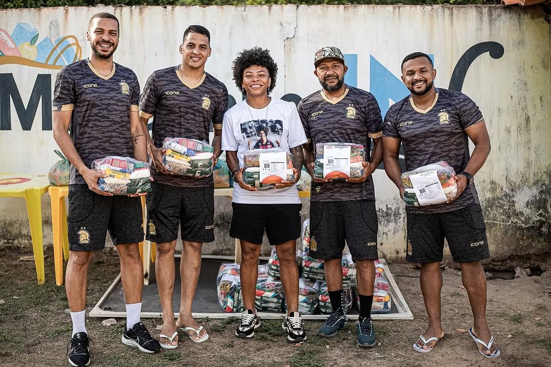 5 pessoas segurando cestas básicas que serão doadas para famílias carentes, 2 homens ao lado esquerdo, Valéria no meio e mais dois homens ao lado direito