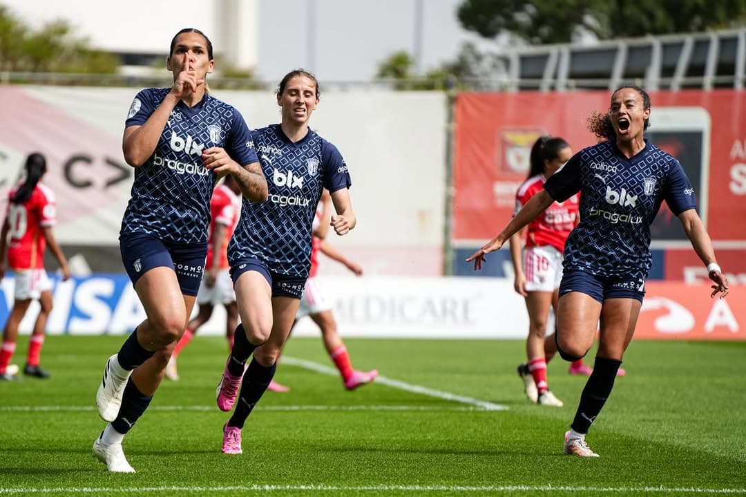 Vitória e mais duas jogadoras comemoram um gol, Vitória está fazendo sinal de silêncio em direção a câmera