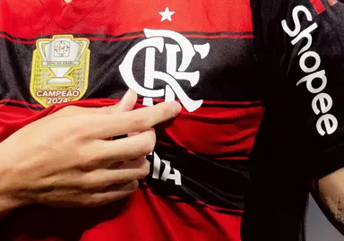 Arrascaeta destaca o escudo do Flamengo ao comemorar um gol; imagem mostra dedos do meia se aproximando do escudo