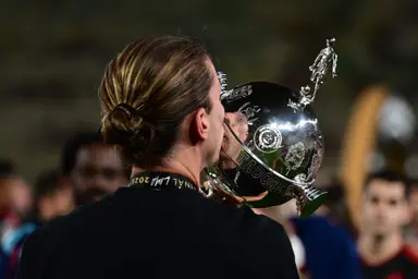 Filipe Luís, de costas, beijando o troféu da Copa Conmebol Libertadores durante a celebração do título de 2025. Ele usa a medalha da final de Lima no pescoço.